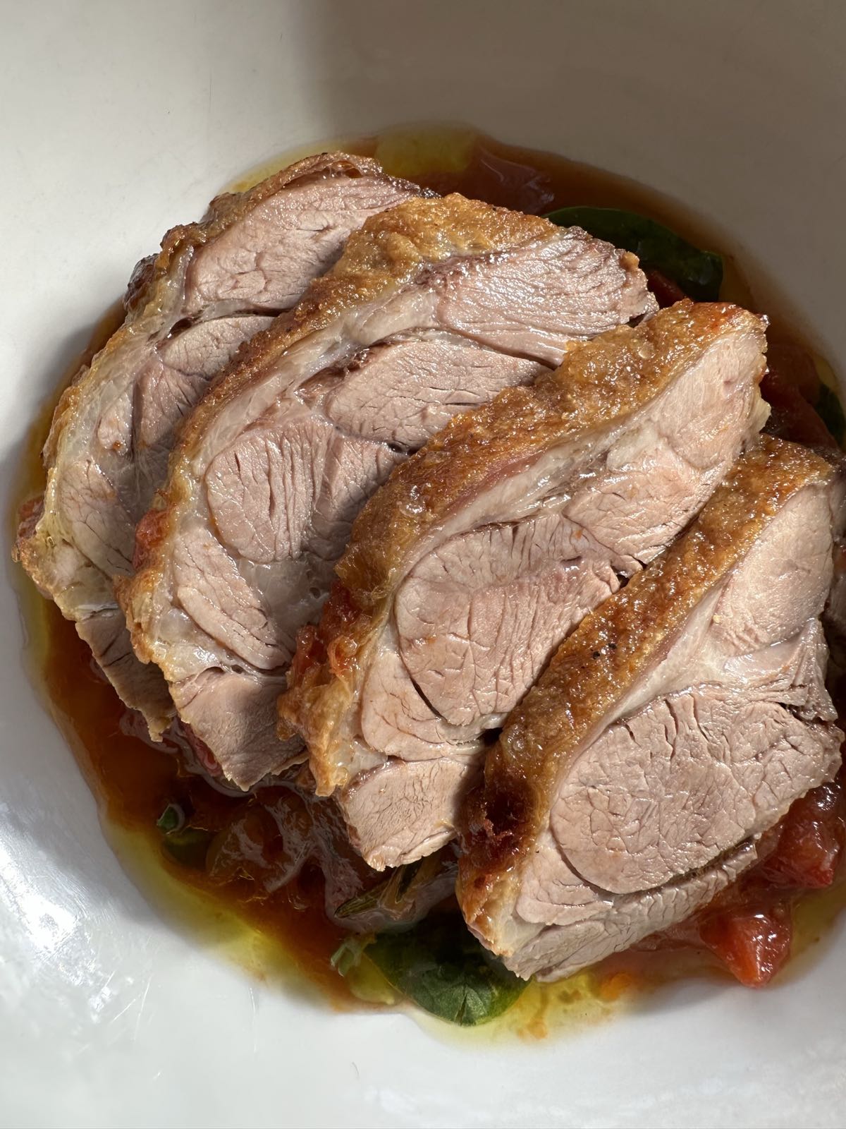 Slices of slow roasted lamb shoulder with crisp golden fat, arranged over tomato and basil ragu in a white bowl