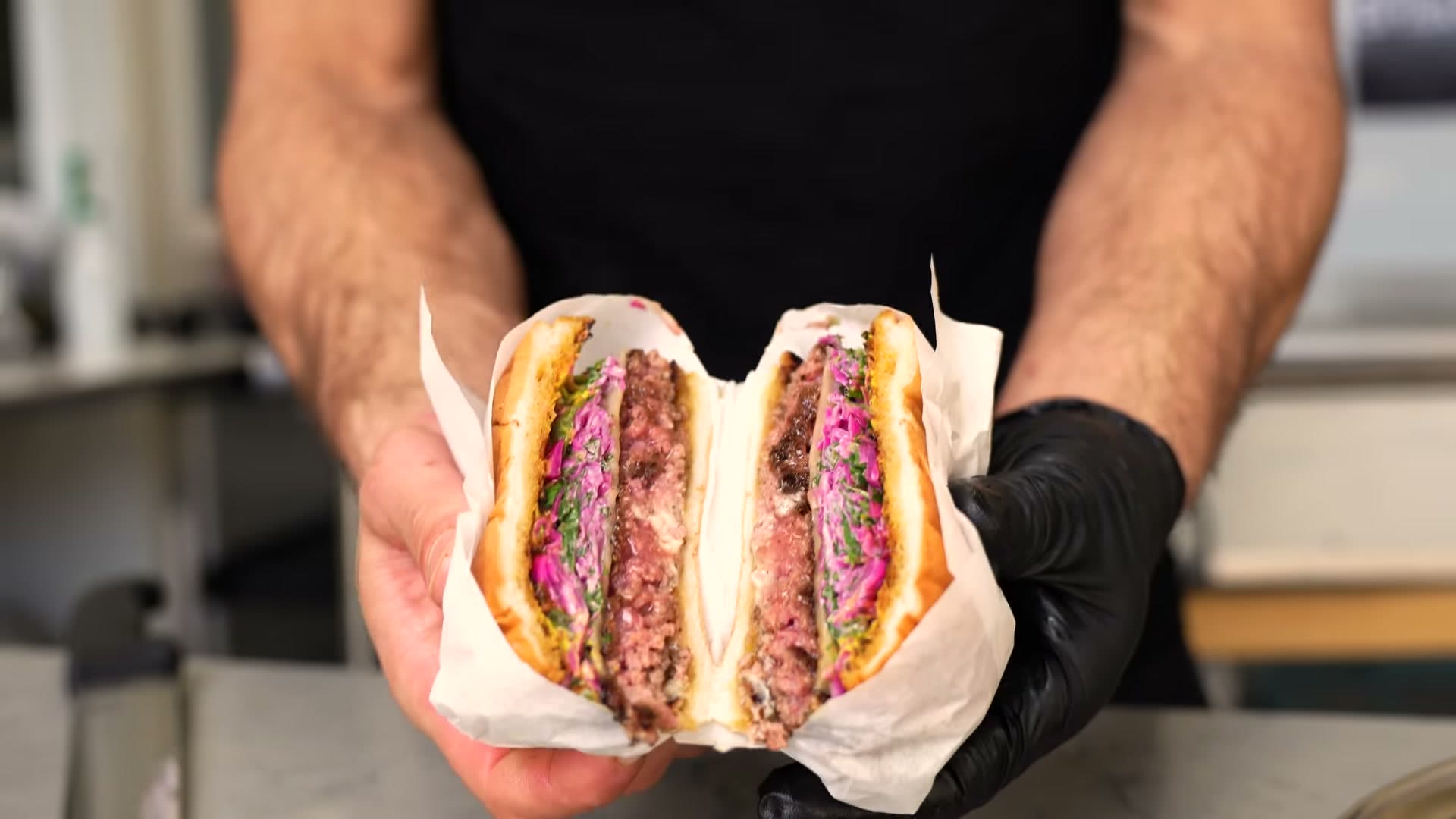 A Wagyu burger cut in half and held in paper, showing the seared patty, melted cheese and red cabbage slaw in a toasted brioche bun